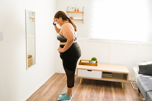 Mujer con sobrepeso estresada usando la báscula de pesaje photo