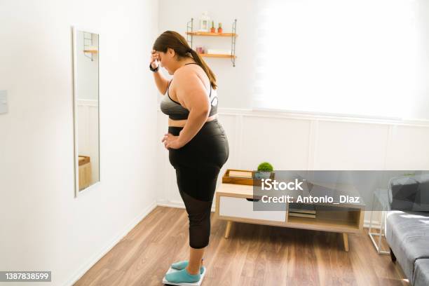 Stressed Overweight Woman Using The Weighing Scale Stock Photo - Download Image Now - Obesity, Overweight, Dieting