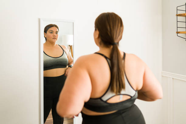 Overweight woman wants to lose weight Losing weight for my health. Worried young woman with obesity dieting and looking herself in the mirror voluptious stock pictures, royalty-free photos & images