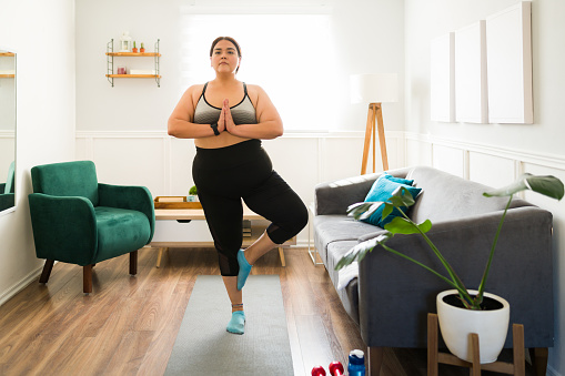 Practicing yoga at home. Big young woman doing a tree yoga pose during a workout