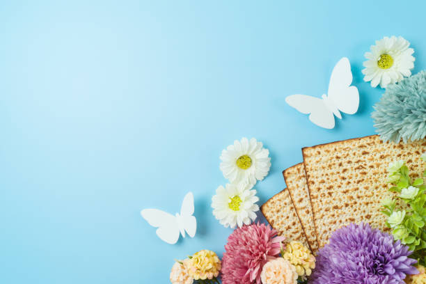 ユダヤ人の休日の過越祭のお祝いのコンセプトは、青い背景にマツァと春の花があります。フラットレイ、上面図 - matzo passover food judaism ストックフォトと画像