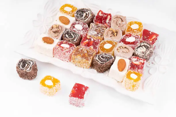 Turkish delight on a plate. Assorted Turkish delight with nuts and sprinkles on a white plate against a light background.