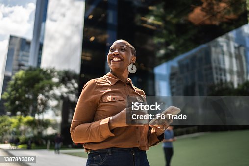 istock Business woman holding smartphone and looking away outdoors 1387843089