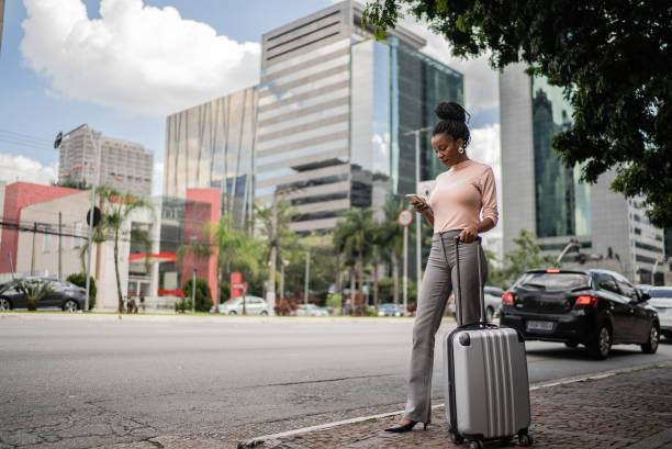 femme d’affaires avec des bagages attendant un taxi à l’extérieur - valise à roulettes photos et images de collection