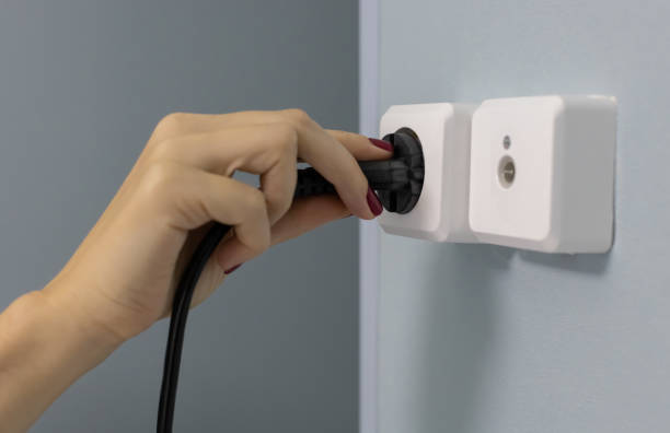 istock a woman's hand sticks a power cord into an electrical outlet 1387843919