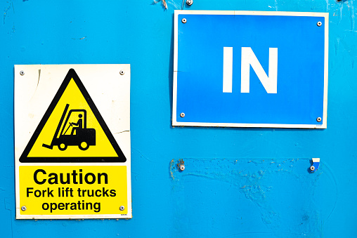 Saturated colours of a generic forklift caution sign seen located at the entrance to an industry facility. The blue painted panel is on the entrance gate to the facility