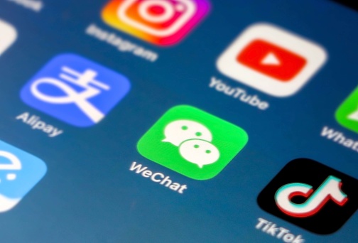 Extremely Popular Chinese social media, multipurpose and instant messaging platform -  WeChat's Application Icon in focus on iPhone smartphone screen, other apps (Tik Tok, Alipay, Instagram etc) out of focus on blue gradient background wallpaper