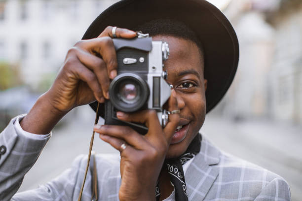 istock Smiling african guy using vintage photo camera outdoors 1387852488