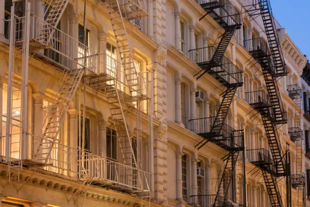 Photo of Facades of Soho loft buildings with fire escapes at dusk. Lower Manhattan, New York City