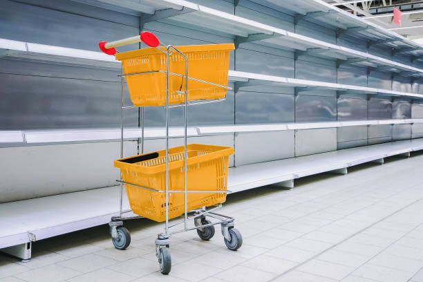 istock Shopping trolley with against empty shelves in grocery store 1387857876