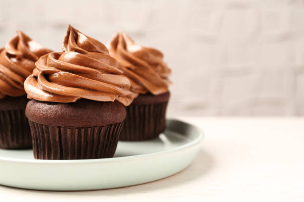 istock Delicious fresh chocolate cupcakes with cream on white table, closeup 1387857910