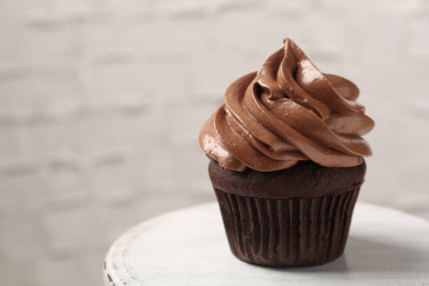 istock Delicious chocolate cupcake with cream on white table, closeup. Space for text 1387858696