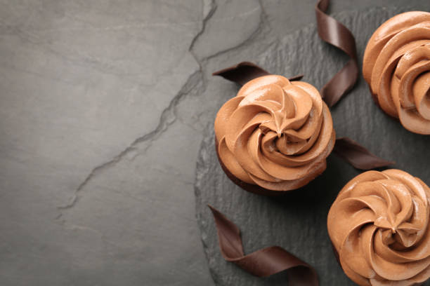 istock Delicious fresh chocolate cupcakes on black slate table, top view. Space for text 1387858703