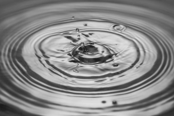 istock Macro view of falling drops on water surface isolated on black and white background. 1387862237