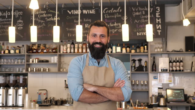 Portrait of bearded hipster barista or bartender wearing apron and looking at camera