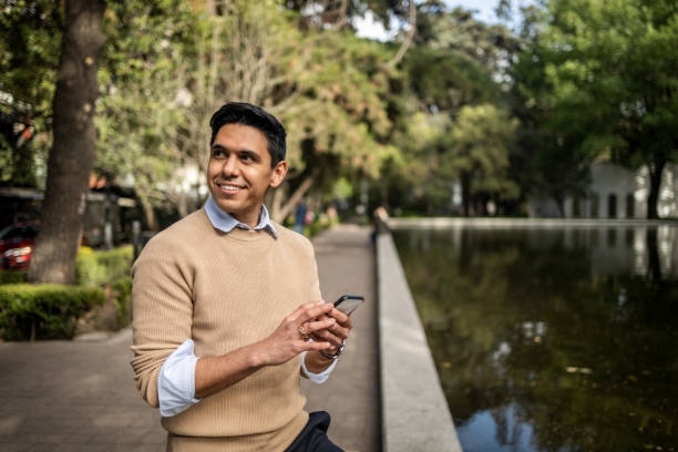 Businessman standing at park and using mobile phone Young man standing next the fountain and using mobile phone businessman happiness outdoors cheerful stock pictures, royalty-free photos & images