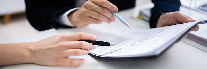 Two Businesspeople Hand Analyzing Document Over Glass Desk