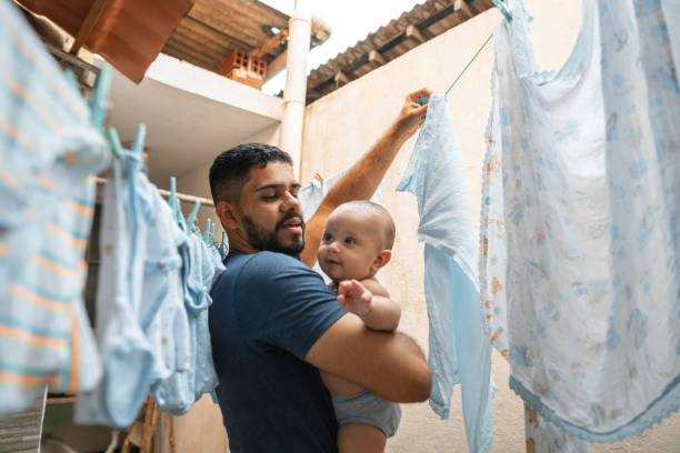 Father hanging clothes on clothesline while taking care of baby stock photo