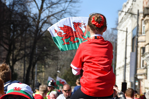 Cardiff, Wales - March 2022: Young girl sitting on her father's shoulders waving the Welsh flag