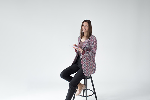 Portrait of business woman in a formal suit sitting on a chair with a notebook in her hands on an isolated white background
