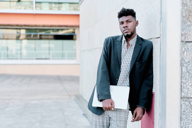 istock african-american businessman leaning against a wall with a laptop computer. copy space for text. 1387877694