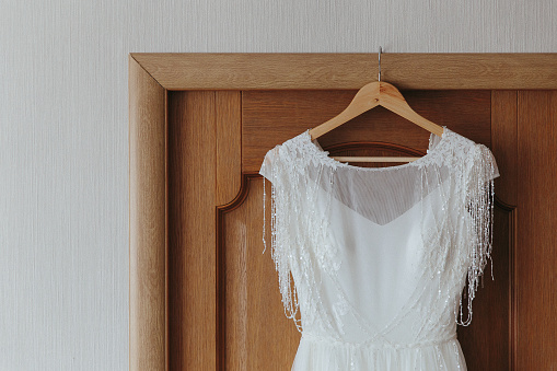 The wedding dress is hanging on a hanger on the door