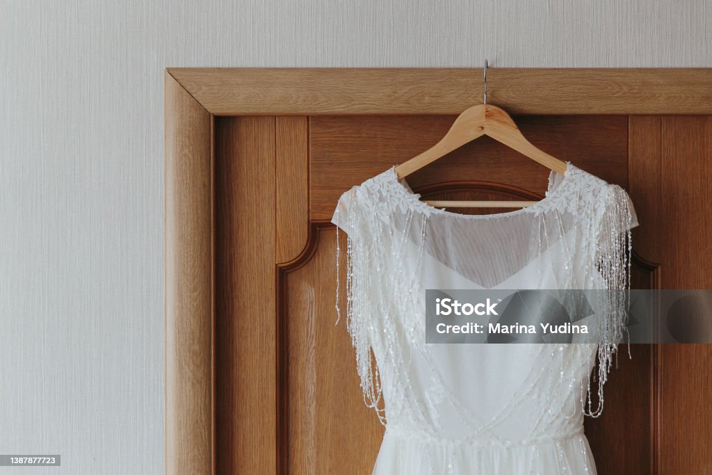 The wedding dress is hanging on a hanger on the door Wedding Dress Stock Photo