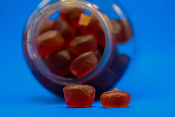 Gummy Pill Bottle Spilled Over with Two Gummy Pills Fallen Out Plastic bottle full of gummy vitamins sideways with gummies falling out in front of blue background. gummy candy stock pictures, royalty-free photos & images