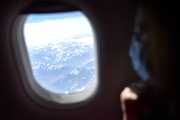 istock Coronavirus mask covering passenger face looking through a window inside airplane 1387895897