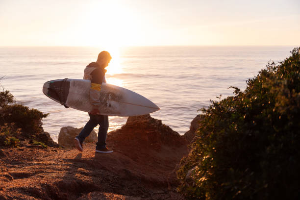 istock man walking at sunset with a surfboard by the sea 1387900558