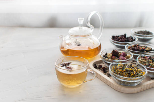 istock Glass cup with hot tea and a kettle on a bright table by the window Tray with different varieties of herbal tea on a white background Delicious and healthy drink Banner Space for text 1387900656