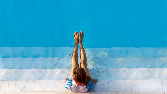 Top view of woman tourist enjoying the relaxation at the refreshing blue crystal clear swimming pool on summer vacation in luxury tropical resort