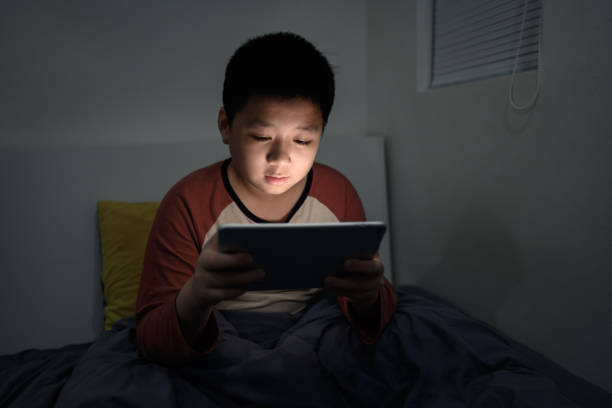 istock An Asian boy is lying in bed playing tablet computer 1387909102