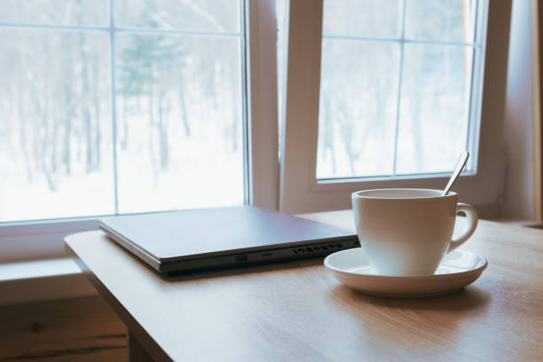 istock Cup and laptop on the table in front of the window. 1387911721