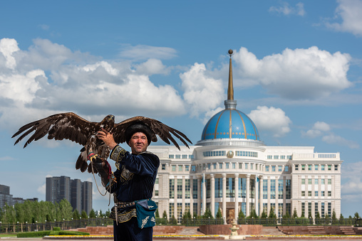Nur-Sultan, Kazakhstan. 07.07.2018. A hunter (berkutchi) with a golden eagle against the background of the residence of the President of Kazakhstan Ak Orda in the city of Nur-Sultan