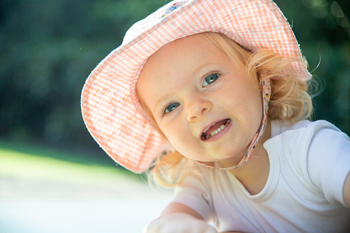 Young girl, baby or toddler playing outside wearing a hat with a wide brim. Happy smiling laughing girl playing on equipment, climbing, at daycare or day care. Happy child playing in the backyard.