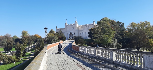 Lublin, Poland - October 9, 2021: The Royal Castle of Lublin (Polish: Zamek Lubelski) seen from the bridge linking the castle with the Old Town of Lublin, Poland. The Royal Castle of Lublin was built in the 12th century and currently houses the Lublin Museum. A man is crossing the bridge carrying a baby stroller.