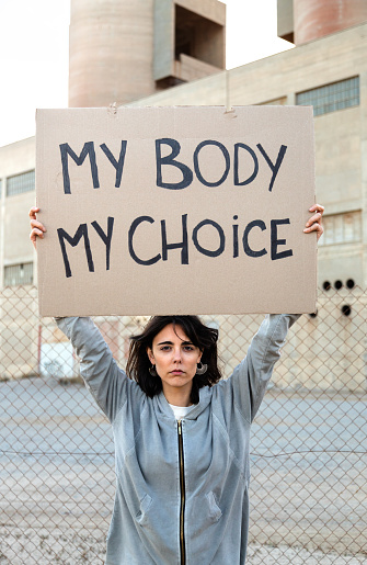 Vertical portrait of young caucasian woman looking at camera with serious expression holding a cardboard sign: My body my choice. Feminism activist concept.
