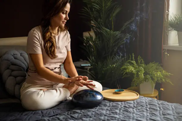 Spiritual yoga woman playing melody on glucophone practice mindfulness harmony balance at bedroom. Yogi female use authentic percussion drum sitting in lotus position relaxing at comfortable home