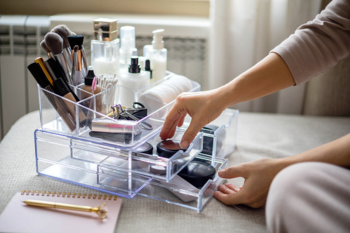 Manos femeninas de primer plano colocando cosméticos de lujo en una caja de acrílico con organización de almacenamiento de cajones photo