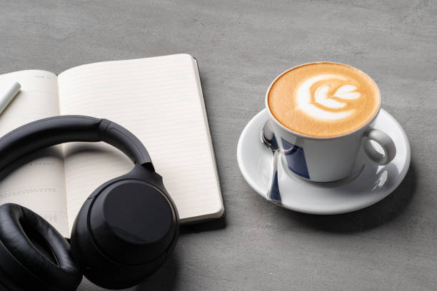 istock Coffee cup with a note book and headphones on gray background 1387936162