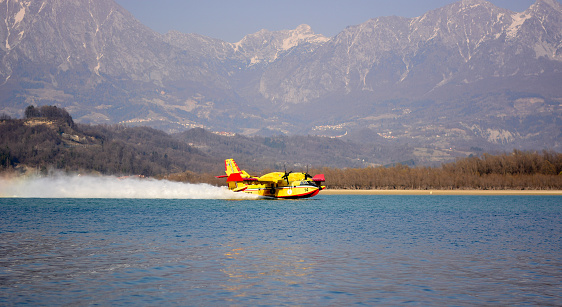 Lake Santa Croce, Belluno, Veneto, Italy, 03/26/2022, a firefighting plane collects water from the lake