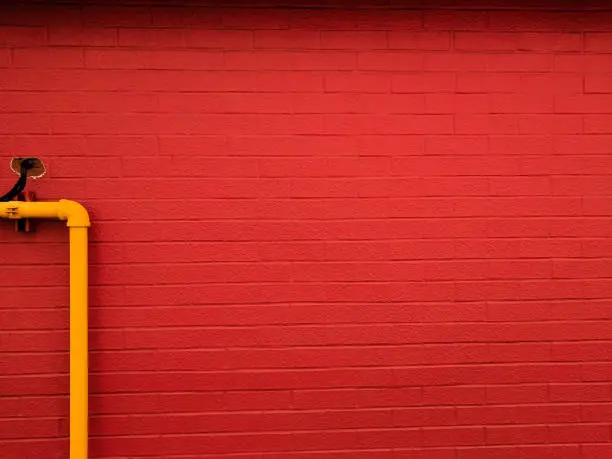 A brick wall paint in red colour and a yellow pipe on left side of the wall