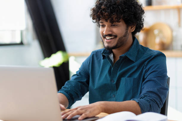 istock Smiling young Indian man freelancer using laptop computer typing working online coworking or modern office Asian student studying from home watching training courses Distance learning online education 1387942892