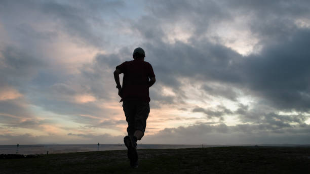 istock Silhouette man running on the beach at dawn, moody cloudy sky. 1387944033