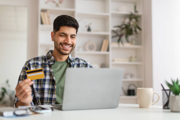 istock Smiling young man using pc and credit card, selective focus 1387944884