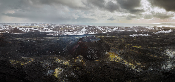 Iceland Fagradalsfjall Volcano Crater and Volcanic Landscape in Winter with Snowcapped Mountains. Panorama view over the volcanic lava landscape of the Fagradalsfjall Volcano on Iceland. Fagradalsfjall Volcano Summit of Langhóll in the Panorama Center. Reykjanes Peninsula close to the city of Reykjavík. Drone Point of View Winter Panorama Landscape Shot. Fagradalsfjall Volcano, Reykjanes Peninsula, Geldingadalir, Iceland