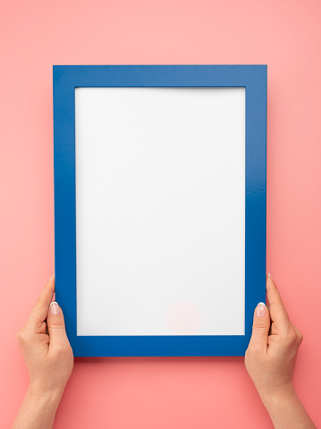 Woman hold blank diploma frame on pink wall background. Female hands hold empty blue mockup frame. Cropped hand of woman holding diploma frame against pink wall. copy space. vertical image