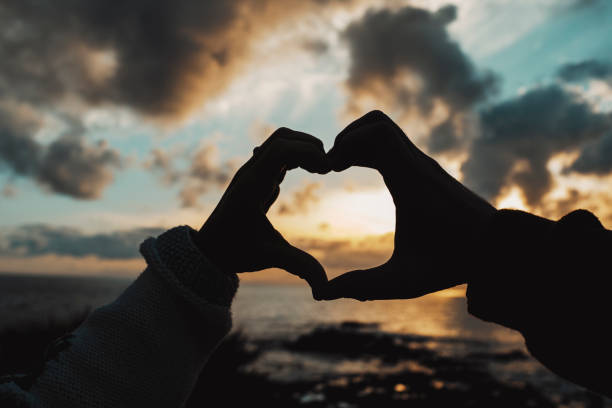 silhouette of heart hands gesture man and woman together in love and relationship against beautiful coloured sunset on the ocean. travel and tourist couple destination peole concept lifestyle - mature couple mature adult heterosexual couple beach imagens e fotografias de stock