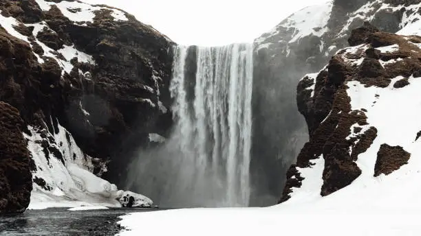 Winter and Snow at Skogafoss Waterfall under overcast cloudscape. Falling water of the Skoga River. Snow and Ice covered Landscape of Skógafoss WQaterfall. The famous Skógafoss is one of the biggest waterfalls in Iceland, with a width of 25m and a drop of 60m. Skógar, Rangárþing eystra, Southern Iceland, Sudurland, Iceland, Nordic Countries, Northern Europe